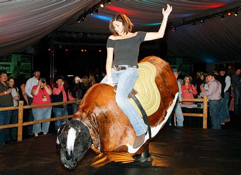 Cool Brunete Girl in Dress Riding on a Mechanical Bull in。